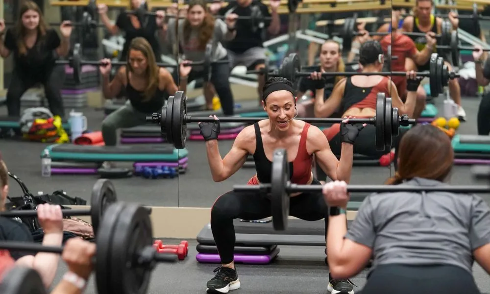 Group of people squatting with barbell over their shoulders.