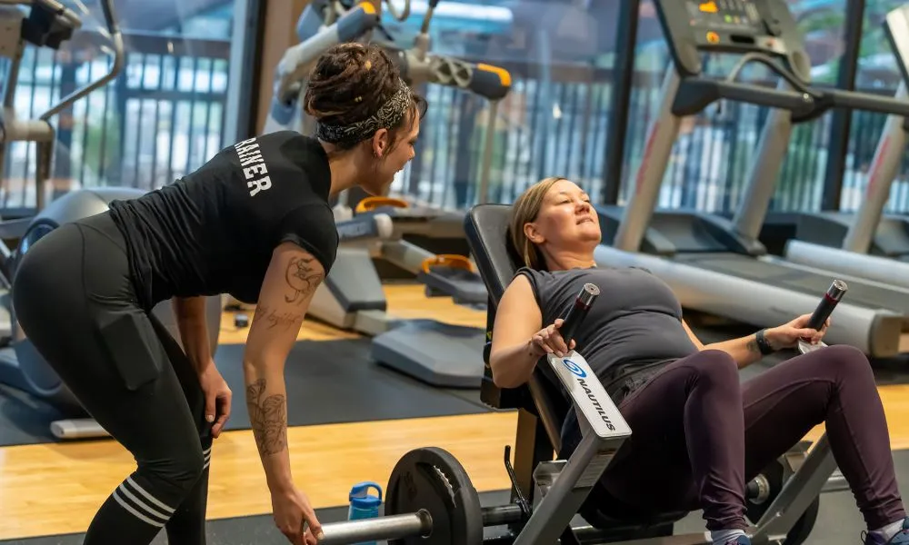 Personal trainer, Lacey, helping client on a workout machine.