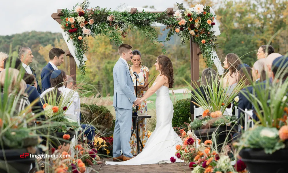 Bride and groom hold hands under floral archway during their ceremony at Ballyowen wedding garden.