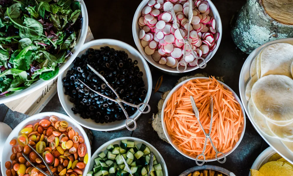 Fresh vegetables in bowls featuring tomatoes, olives, radish, carrots and cucumbers. 