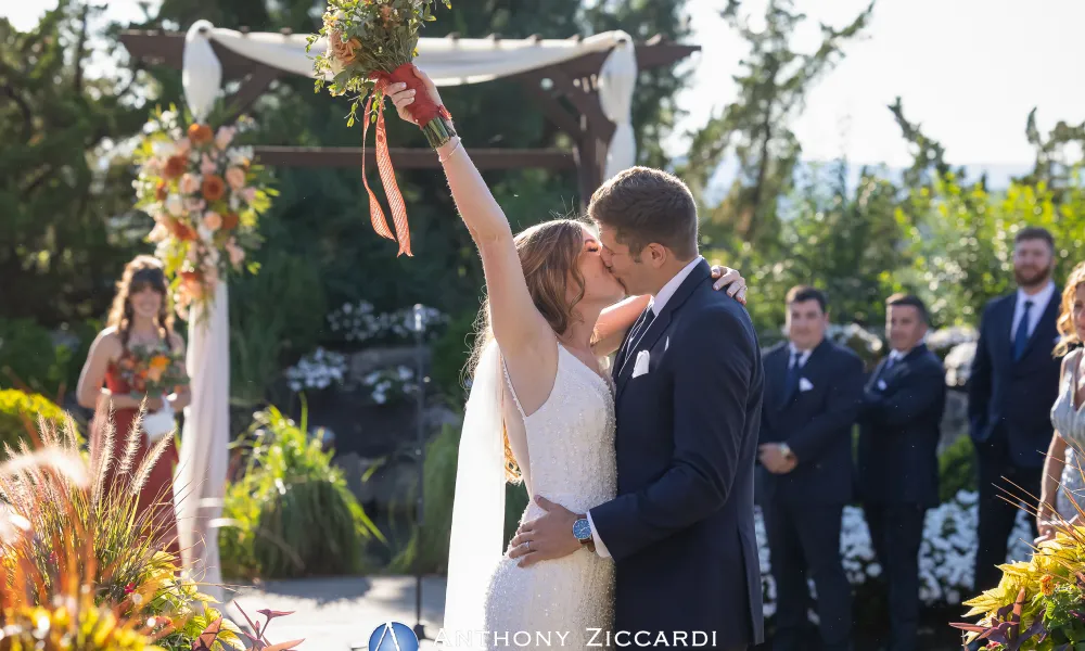 Bride and groom kiss under arch during their Bride walking down the aisle at Wedding Garden ceremony space at Crystal Springs Country Club. 