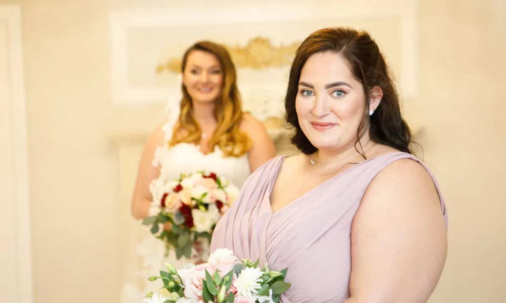 Bridesmaids in purple dress stands in front of bride. 