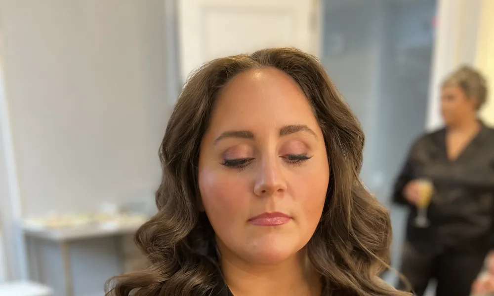 Woman sits with her eyes closed and her hair down styled wavy. 