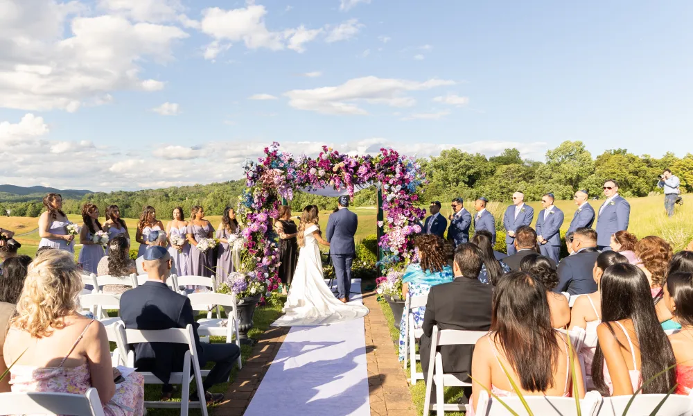 Bride and groom stand under purple flowers during their ceremony at Ballyowen wedding garden.