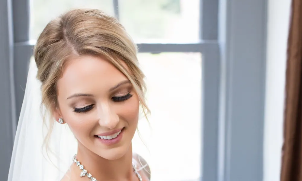 Bride wearing white dress and veil holds bouquet of white flowers. 