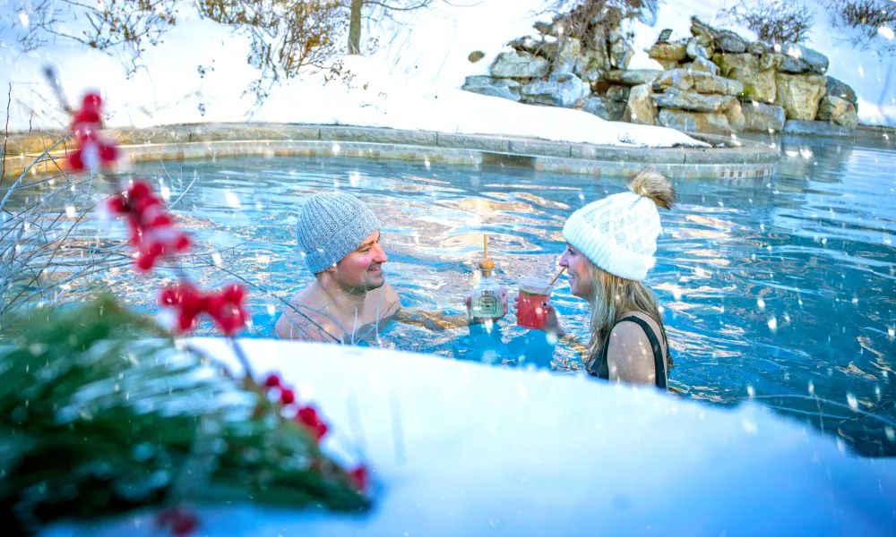 Couple drinks cocktails in outdoor snow pool.