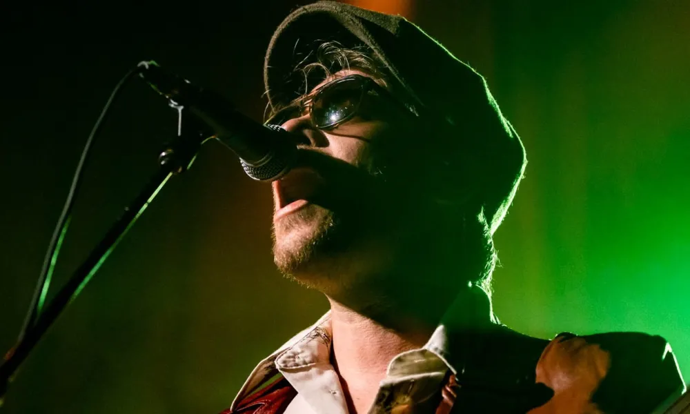 Man wearing hat and sunglasses singing into microphone