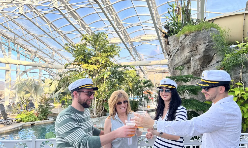 Four people stand with captain hats in Biosphere pool cheersing their drinks.