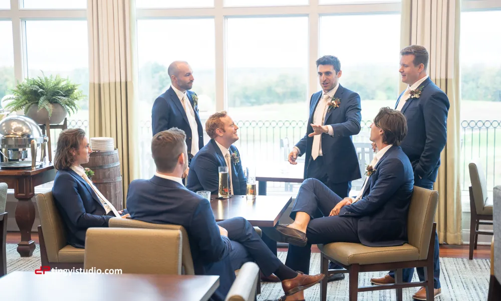 Groomsmen sitting around a table talking in navy blue suits.