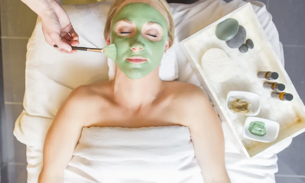 Woman laying on spa table with green mask on her face.