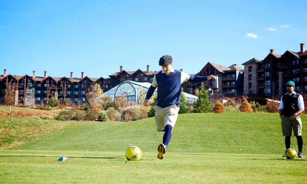 Guy wearing hat kicking a foot golf ball