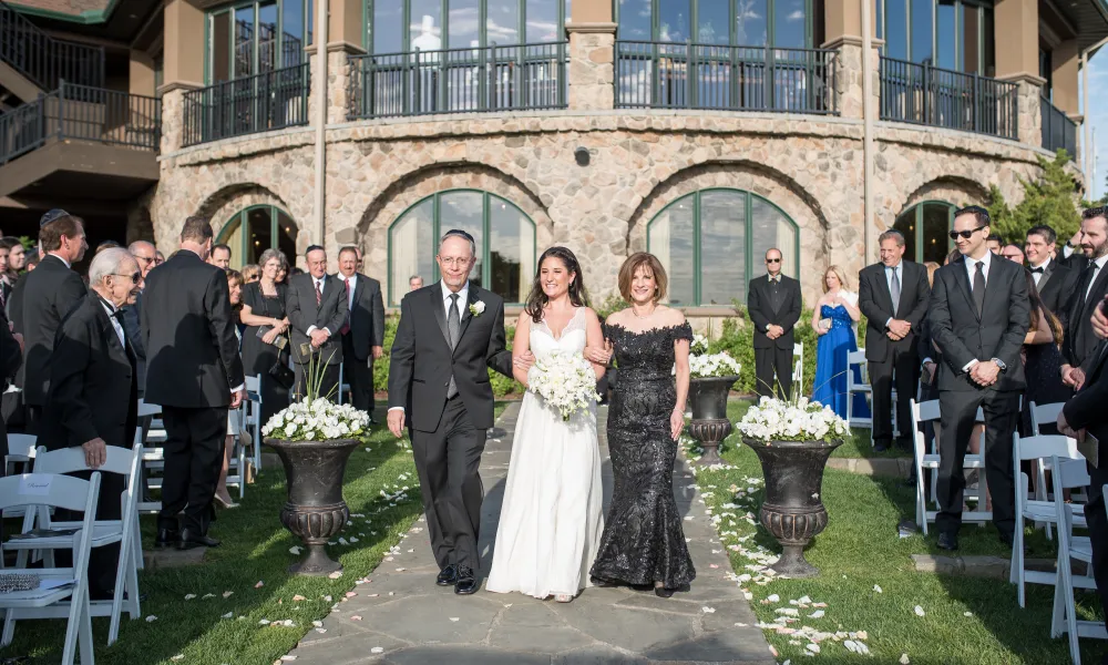 Bride walking down aisle with parents at the wedding garden