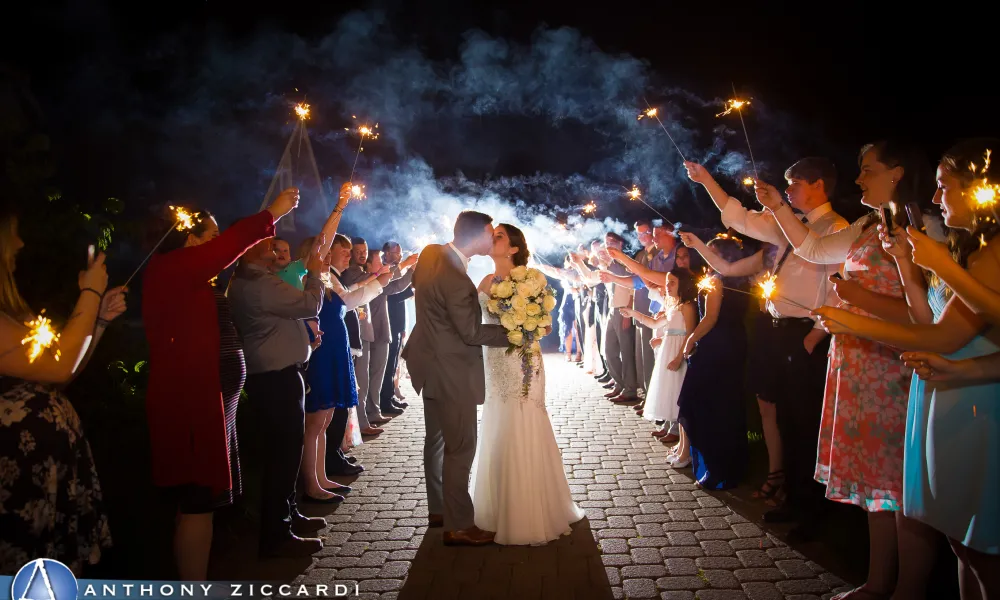 Bride and groom kissing as guests make walkway out of sparklers