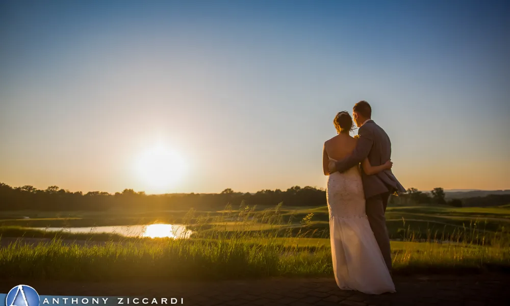 Bride and groom arms around each other looking into the sun