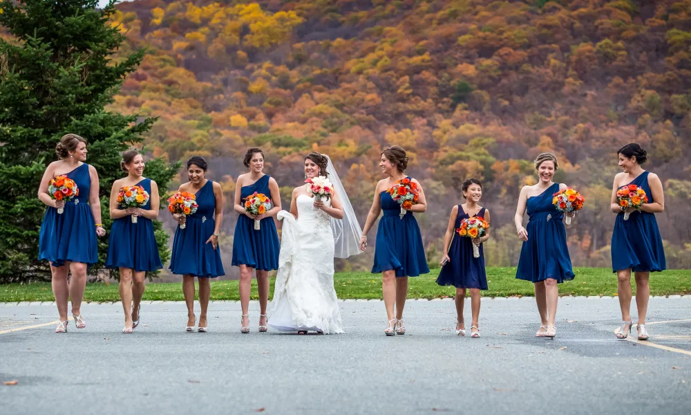 Bride walking with her bridesmaids, wearing short blue dresses, among the fall mountains.