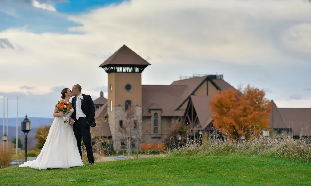 Bride and groom kissing in front of fall foliage and Crystal Springs Clubhouse