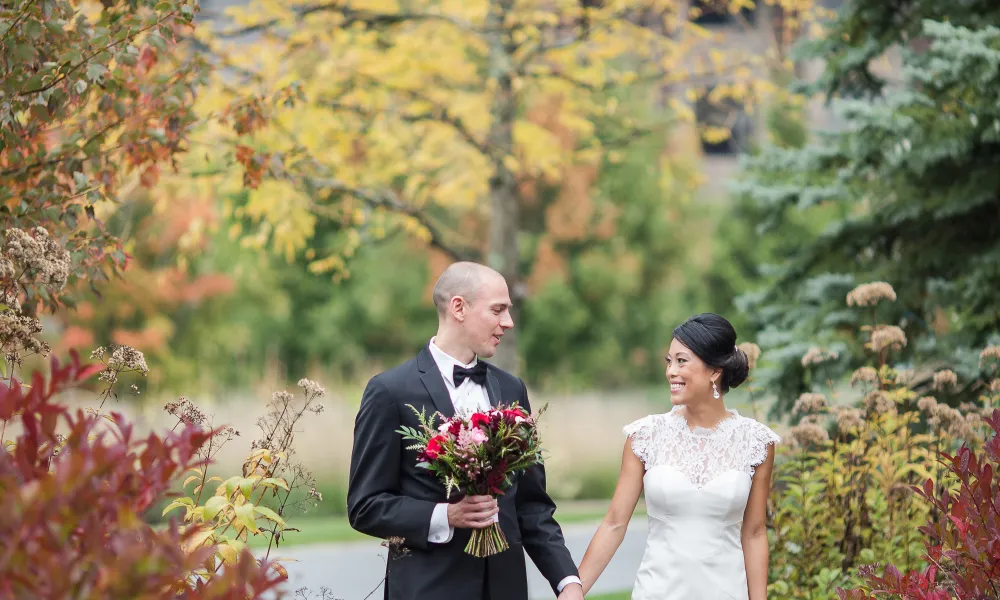 Bride and groom holding hands walking through fall path.