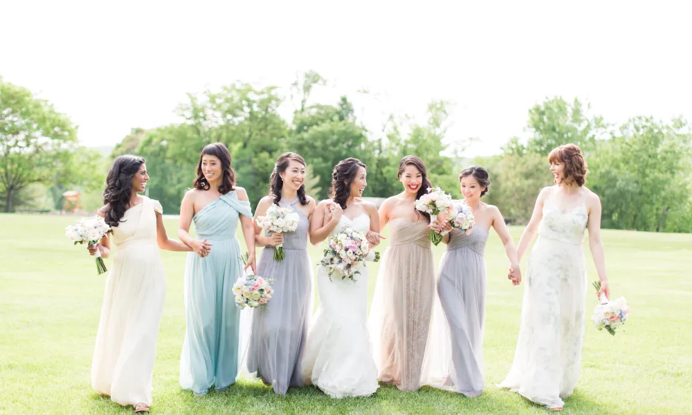 Bridesmaids and bride walk through grass field.