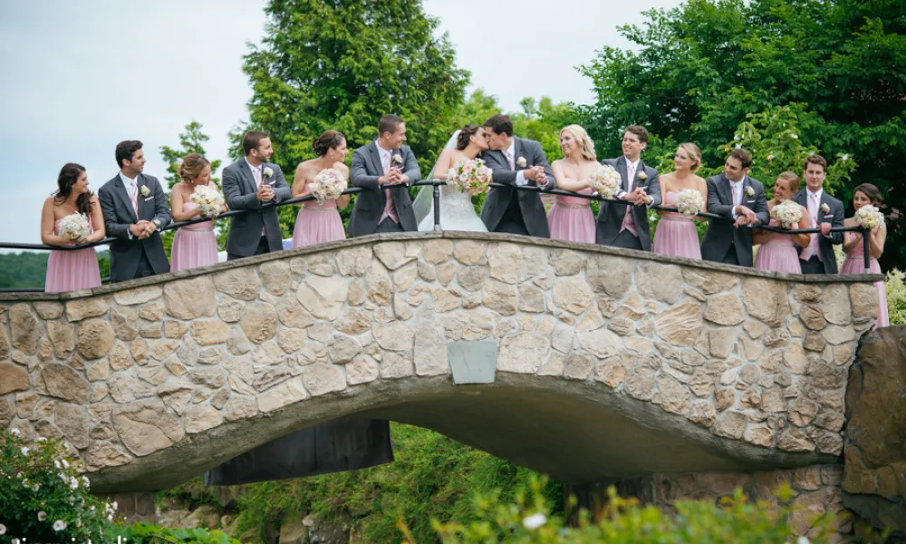 Wedding party stands on stone bridge.