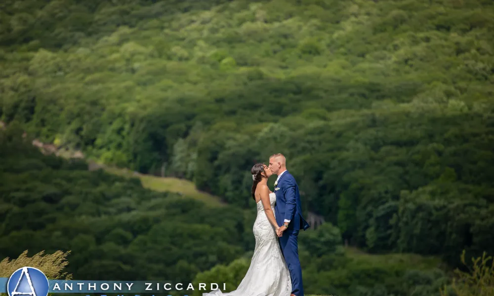 Bride and groom kiss in front of green mountains in background.