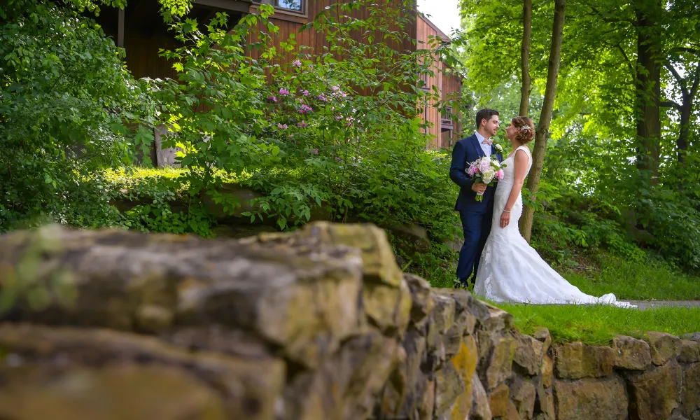 Bride and groom standing amongst green foliage.