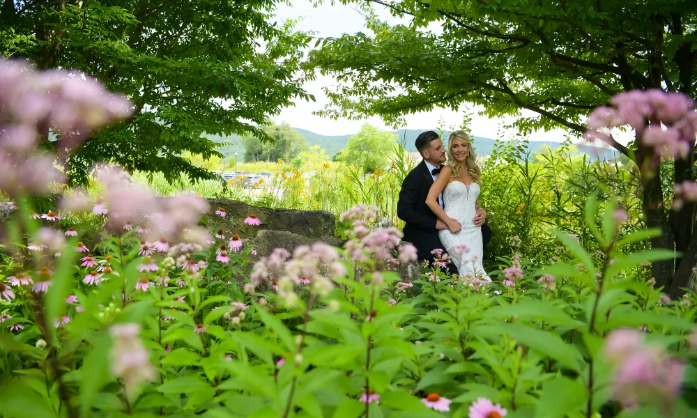 Bride and groom stand between green and pink florals.