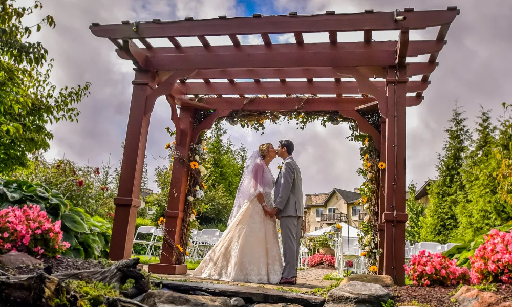 Bride and groom kiss under ceremony arch.