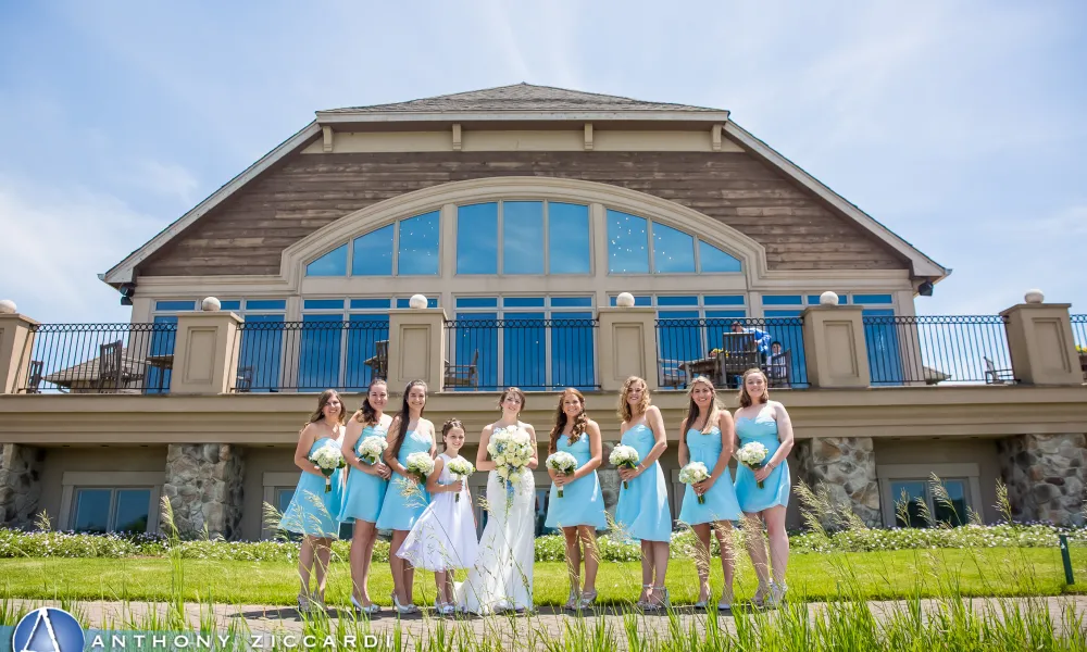 Bridesmaids, wearing short light blue dresses, stand with bride in front of Ballyowen Golf Club.