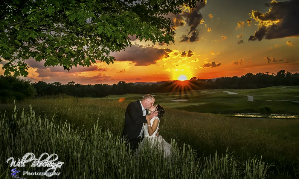 Bride and groom kiss with orange sunset behind them.