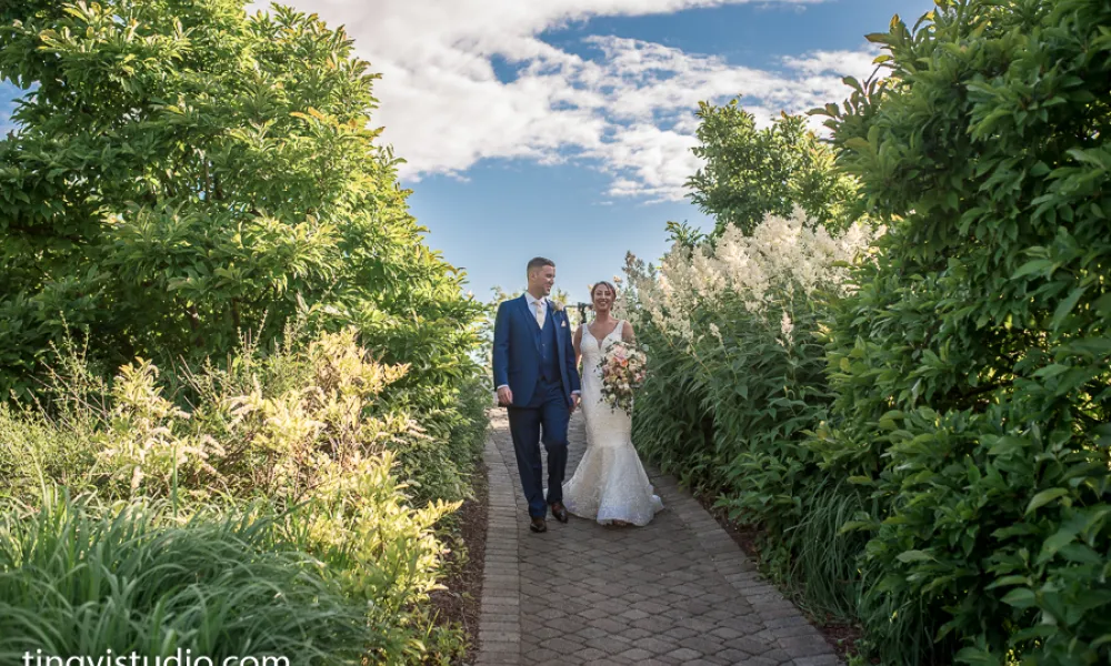 Bride and groom walk down pathway surrounded by greenery.