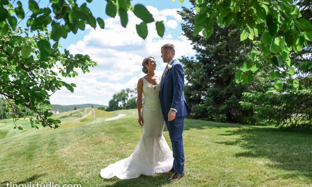 Bride and groom stand side by side between trees.