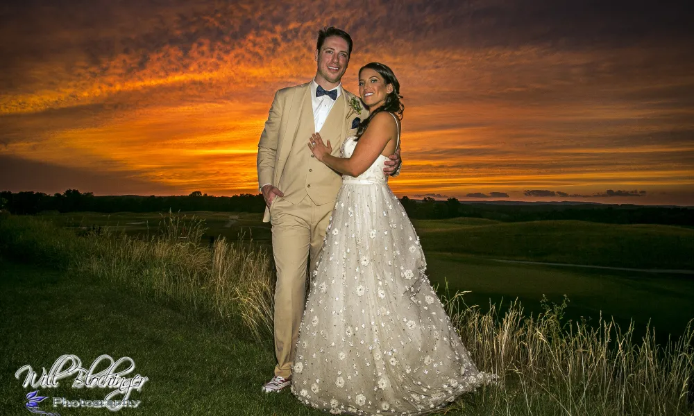 Bride and groom, who is wearing a tan tux, stand in front of orange sunset.