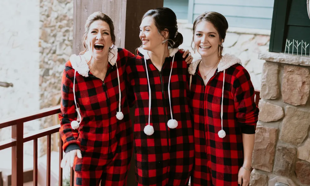 Three women stand together wearing flannel onesies.