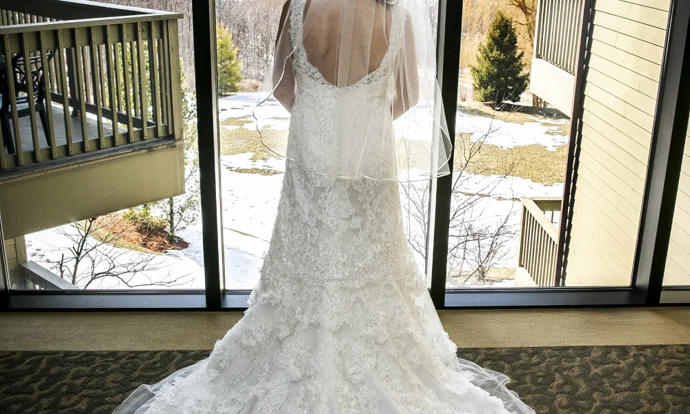 Bride looks out large window to see mountain range in distance.