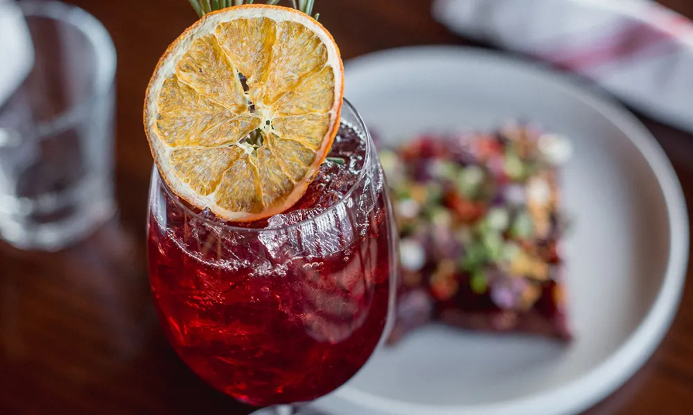 Cocktail topped with rosemary and orange slice.