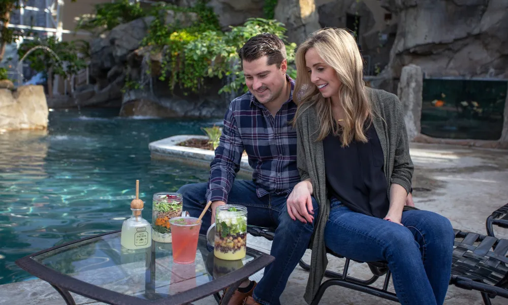 Woman and man sitting pool side in the Biosphere drinking cocktails and eating salads.