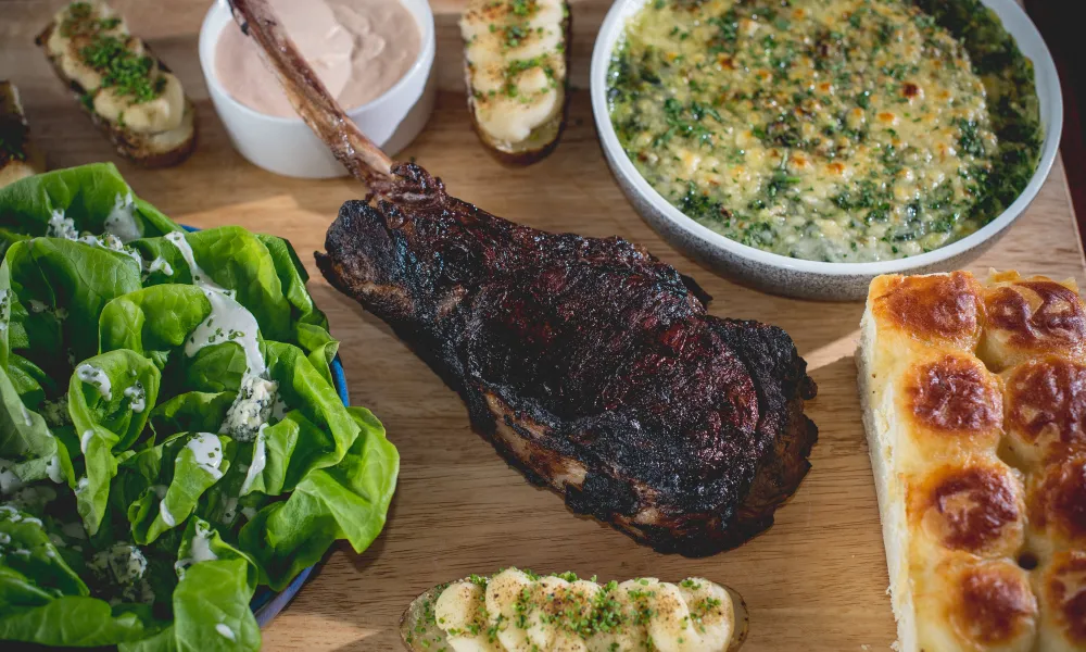 Steak, lettice, bread and more on a wooden platter.