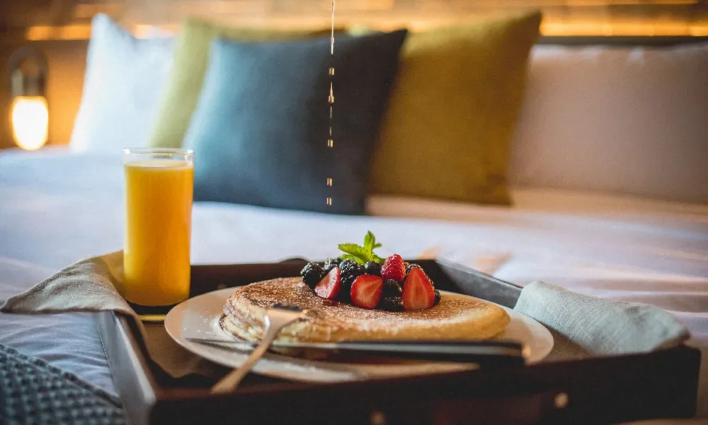 Pancales, fresh fruit and orange juice on a tray in bed.