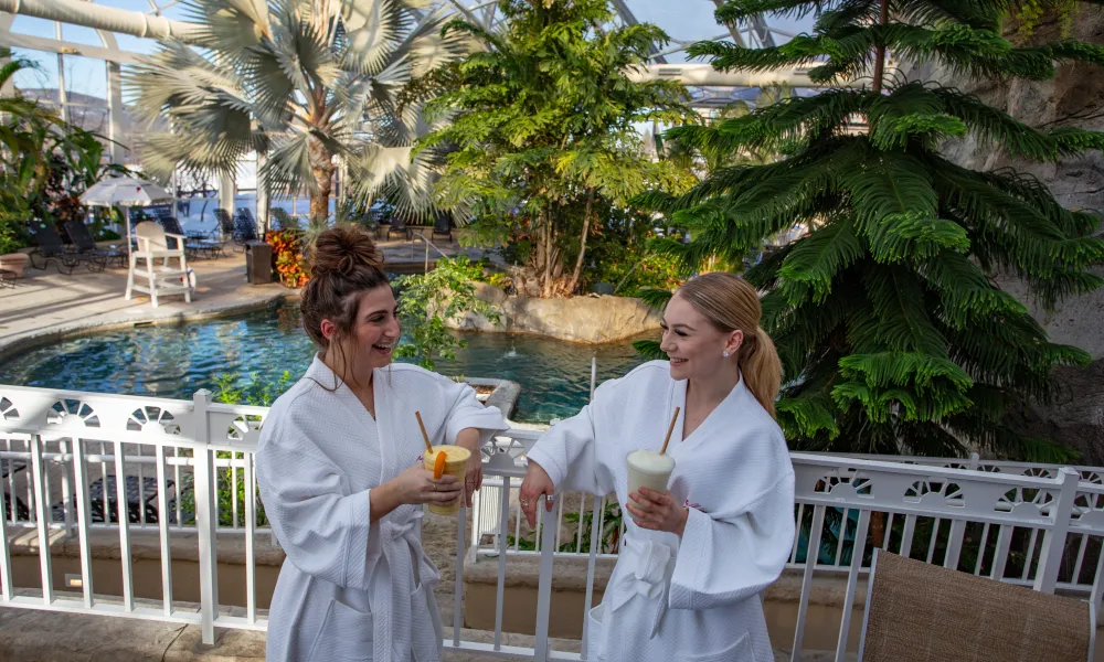 Two women in white robes drinking in Biosphere Pool Complex