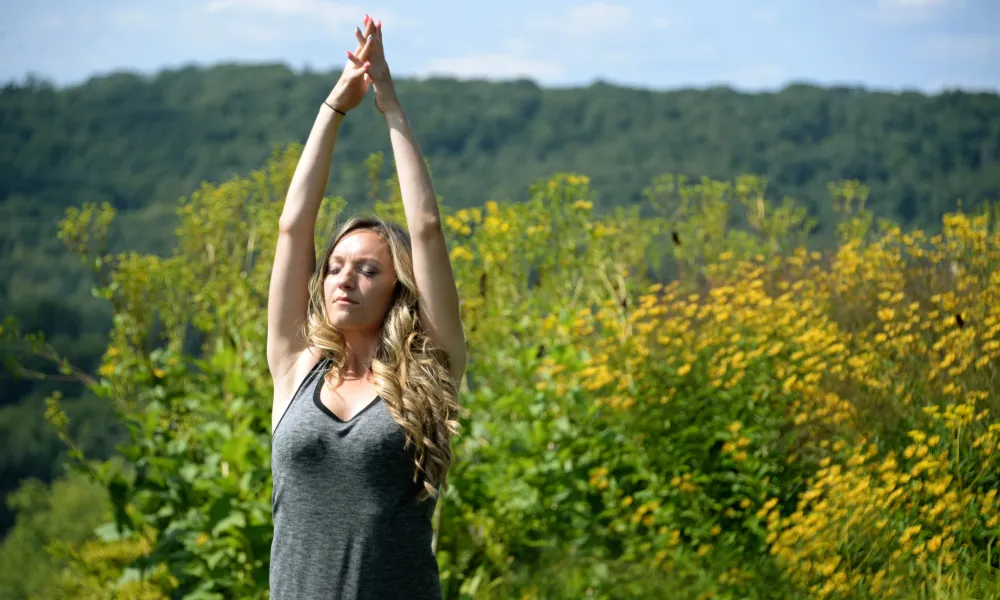 Women stretching with hands upward toward sky standing in front of yellow flowers.