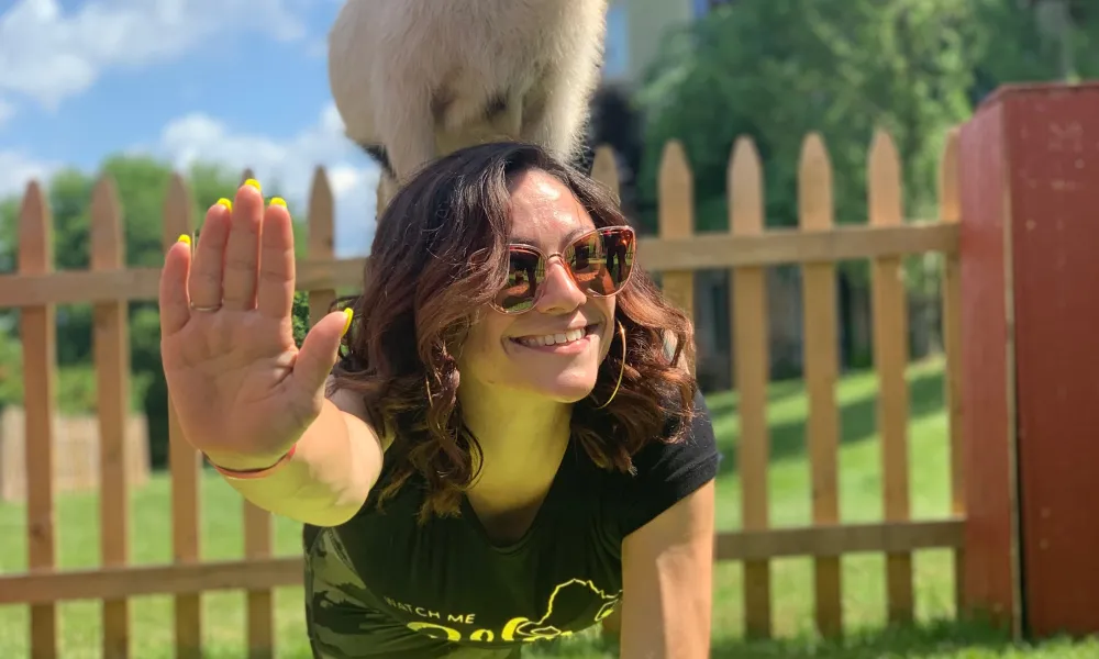 Woman doing yoga pose with goat on her back