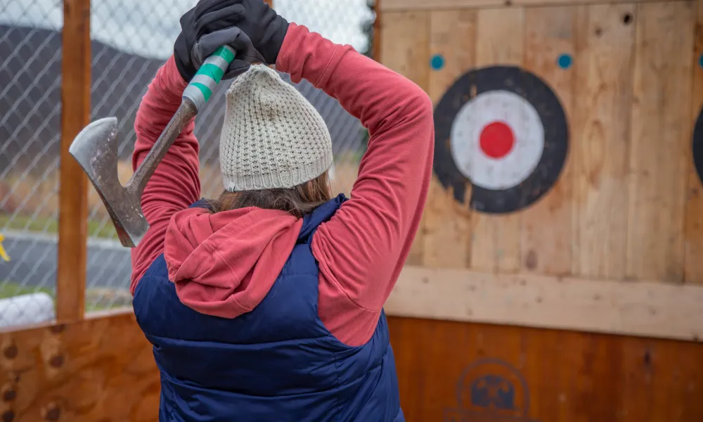 Woman wearing hat and gloves getting ready to throw axe at target.