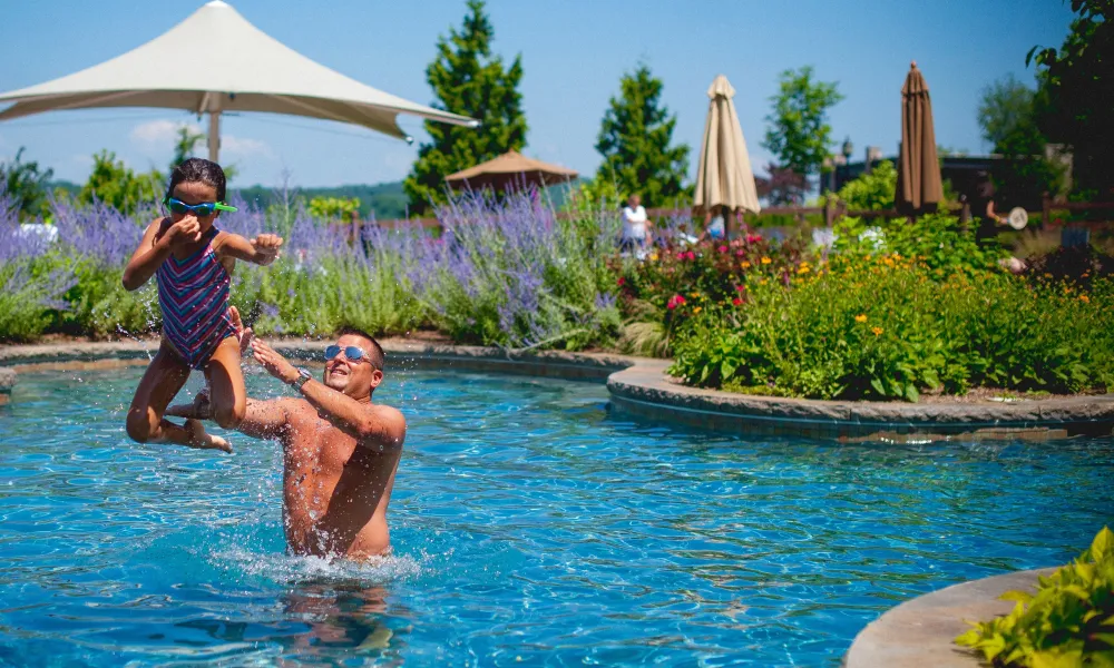 Young girl midair as her father throws her in pool.