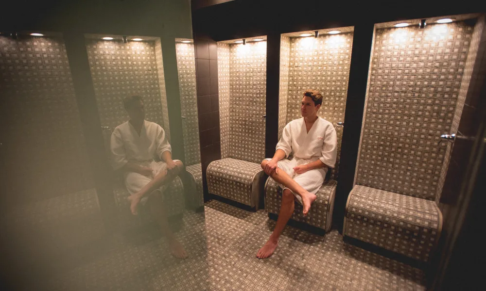 Man in white bath robe sitting in sauna.