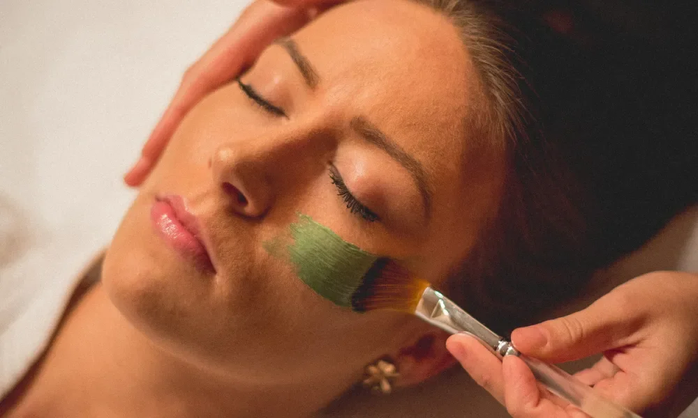 Green face mask being applied to woman's face with brush.