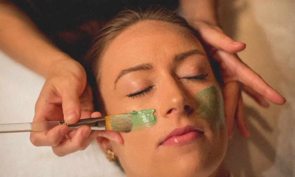 Green face mask being applied to woman's face.