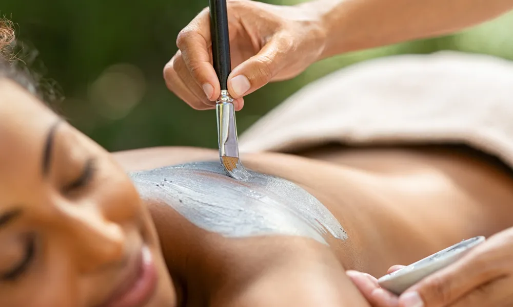 Mud being painted on woman's back for spa treatment.