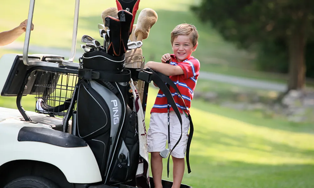 Little boy standing on the back of a golf cart