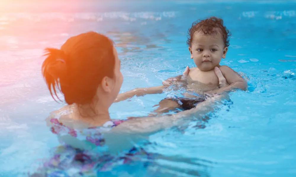 Woman holding baby in pool.