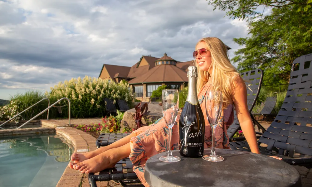 Woman sitting in lounge chair by vista 180 pool with a bottle of prosecco.